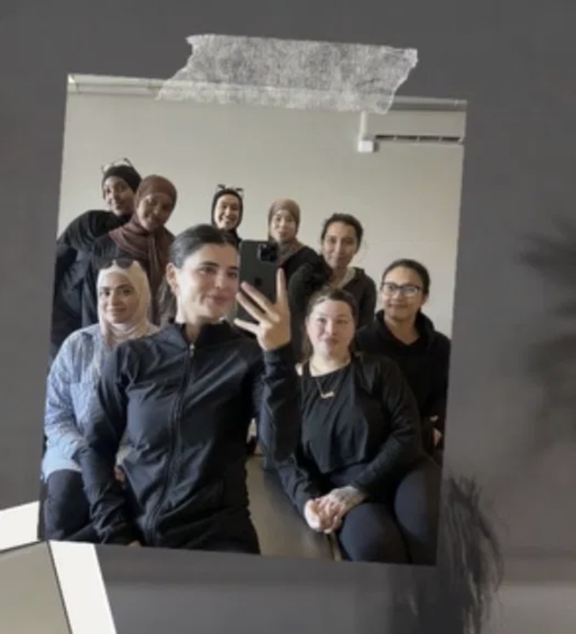 A taped-photo style picture of the group in the studio mirror, Lara at the front holding her phone with the women gathered behind her.