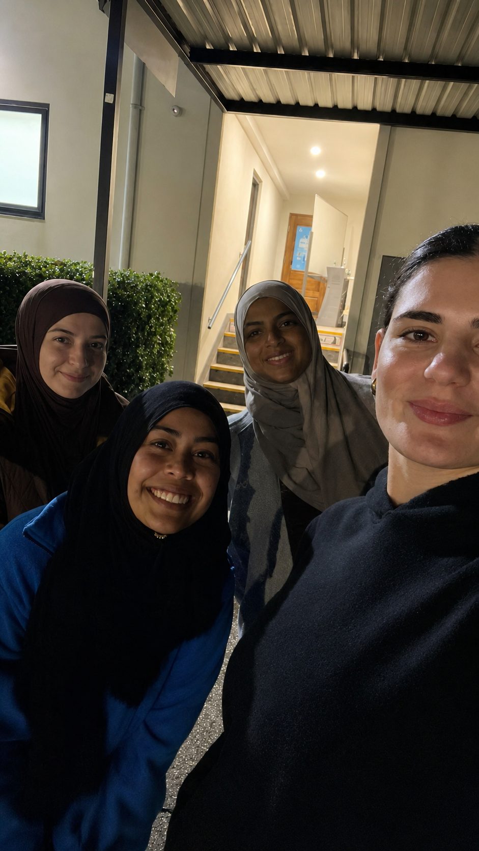 An evening selfie outside the venue entrance: Lara in the foreground with three smiling women beside her under the lit awning.